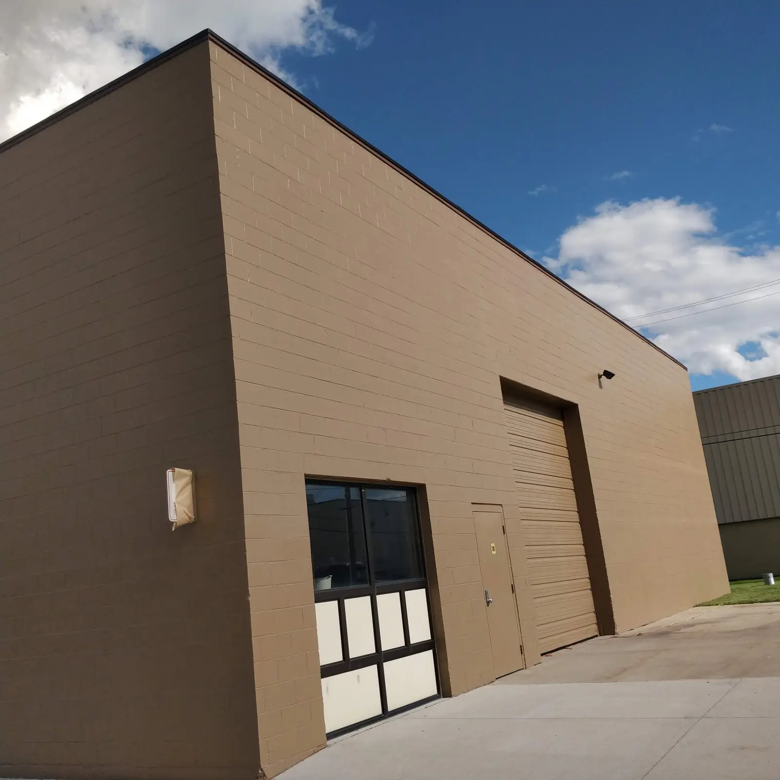 Commercial building exterior painted in a warm taupe with dark brown trim and a roll-up garage door