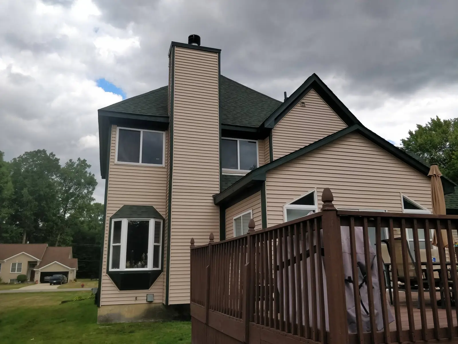 Rear elevation detail of a tan vinyl-sided home with dark green trim and a bay window