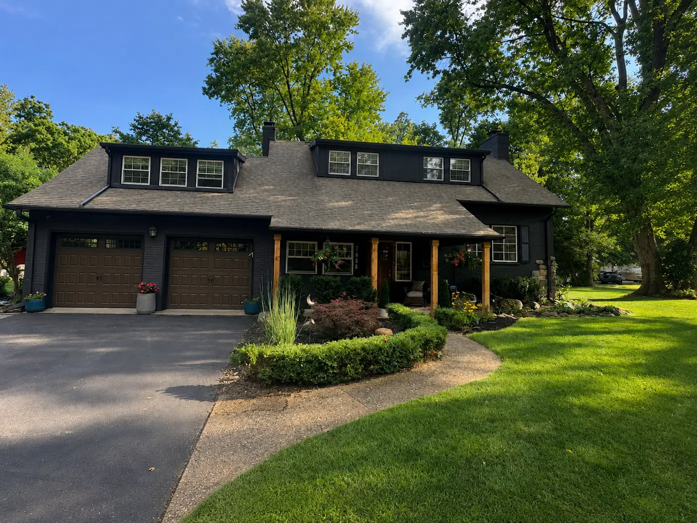 Brick home painted deep charcoal with wood-tone garage doors and lush landscaping
