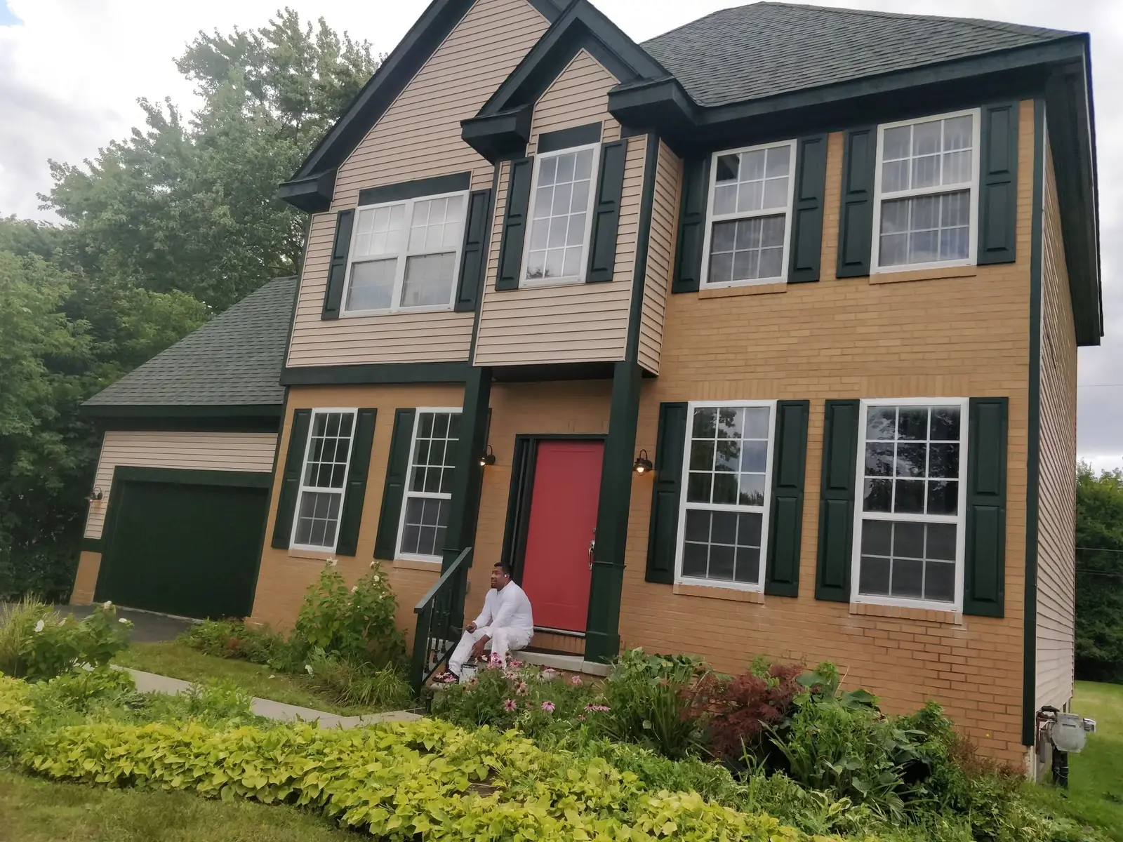 Exterior repaint of a two-story home with dark green trim, tan siding, and a red front door