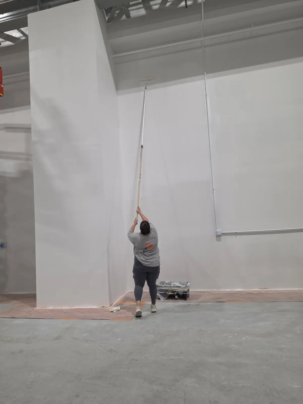Roca's Painting crew member applying coating to a tall facility wall with an extension pole
