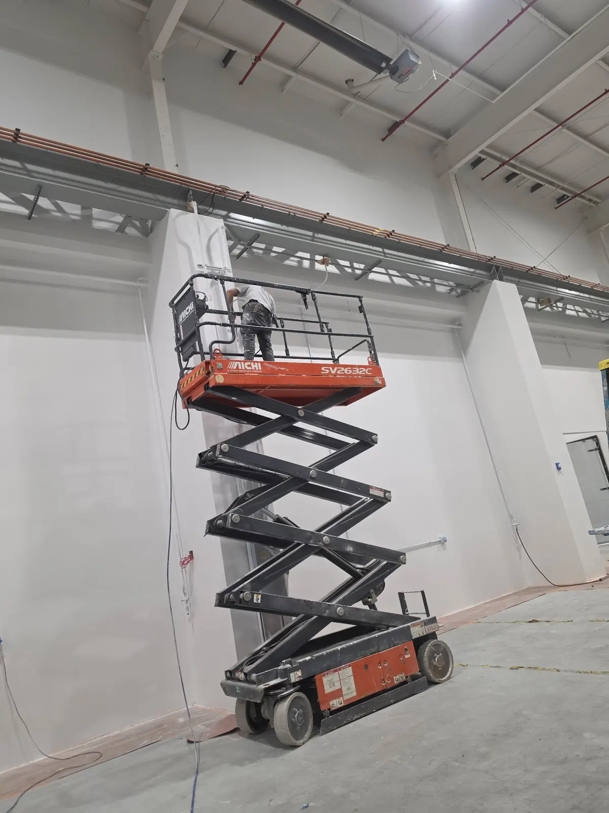 Crew member on a scissor lift working near the ceiling of a commercial facility