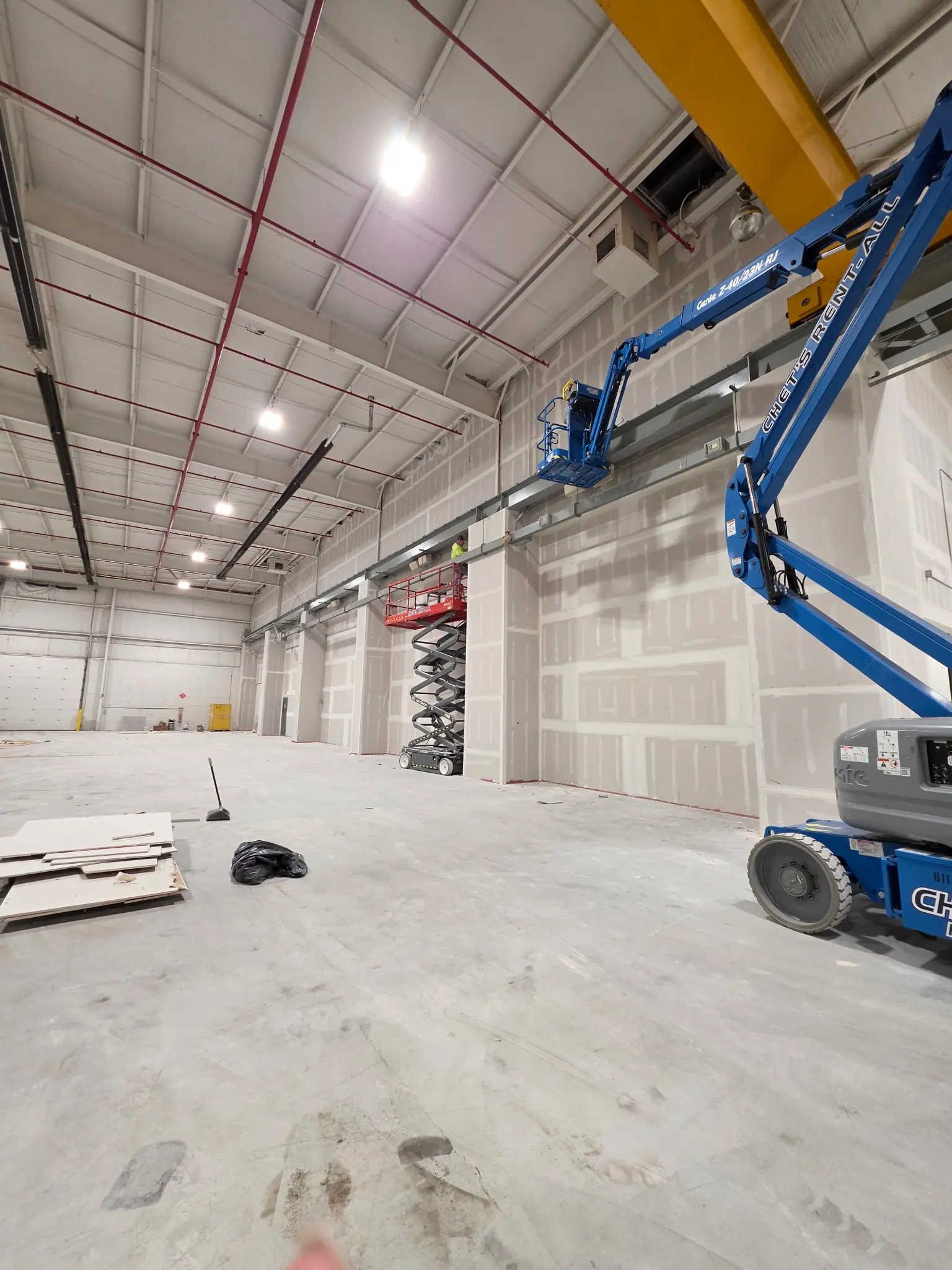 Crew working at height in a large warehouse facility using a boom lift and scissor lift