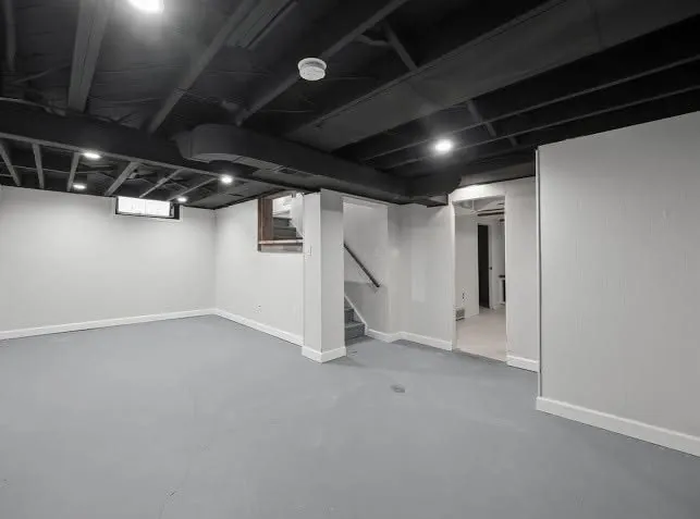 Finished basement with freshly painted charcoal ceiling beams and light gray floor